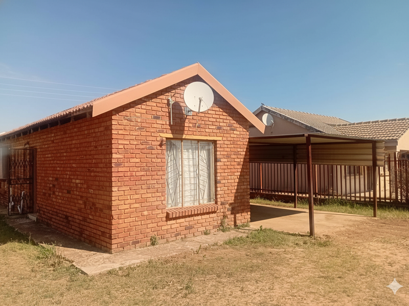 A single-story face brick house featuring a tiled roof, security bars on windows, a side carport, and a secure entrance gate.