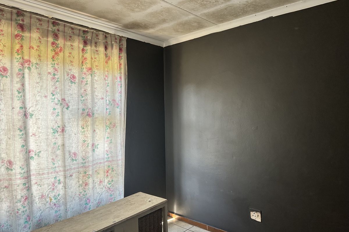 A bedroom featuring dark painted walls, tiled flooring, and visible water damage on the ceiling tiles.