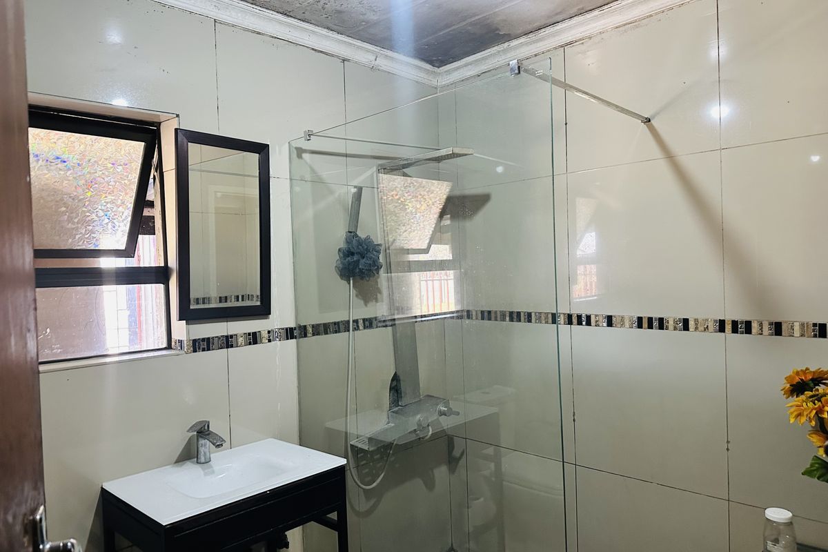A bathroom featuring a glass shower enclosure, vanity basin, and tiled walls, currently showing signs of ceiling water damage.