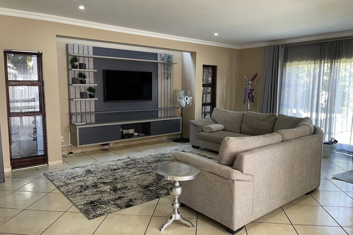 Spacious living room featuring a custom built-in media unit, neutral tiled flooring, recessed lighting, and large sliding doors providing ample natural light.