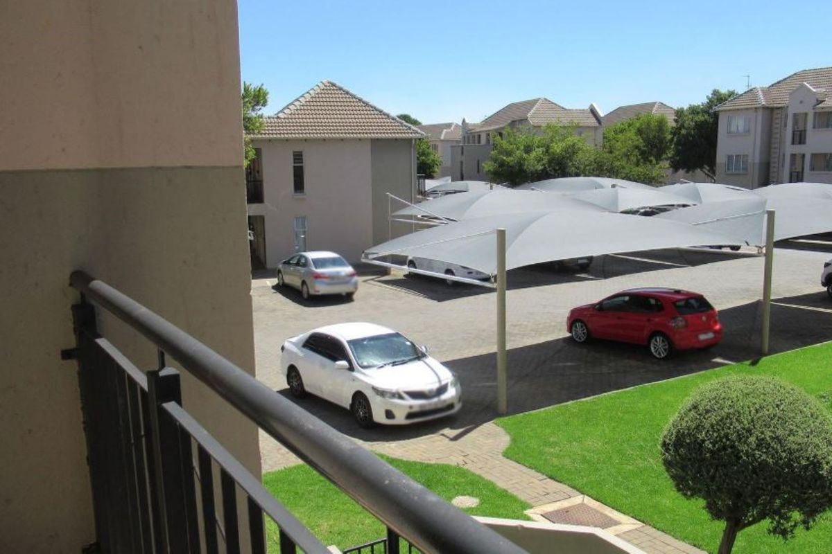 View from a balcony overlooking a paved parking area with shade cloth carports and a well-maintained communal lawn.