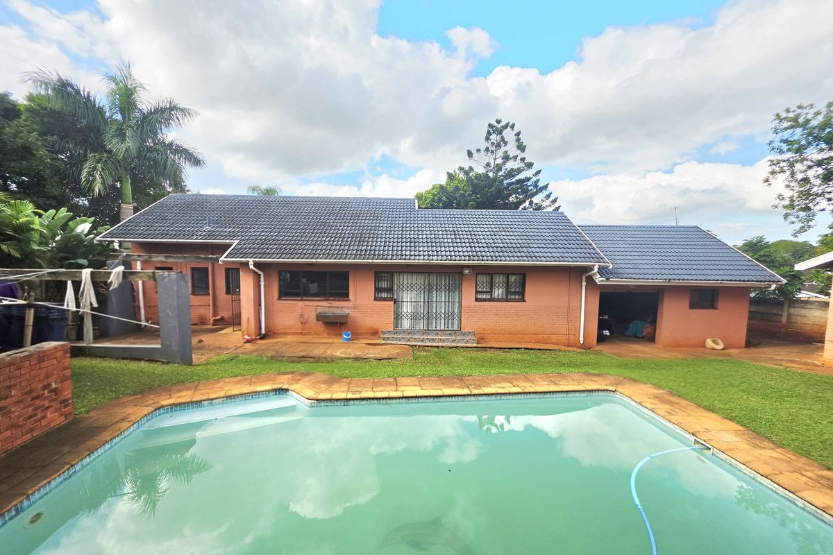 Rear view of the property featuring a swimming pool, paved surround, and a brick facade with a tiled roof and attached garage.