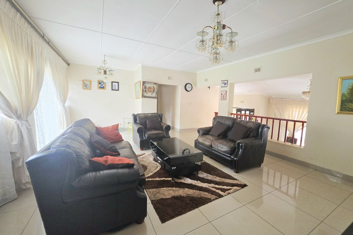 Spacious living room featuring polished tile flooring, decorative crystal chandeliers, and an open-plan layout with a wooden balustrade overlooking an adjacent area.