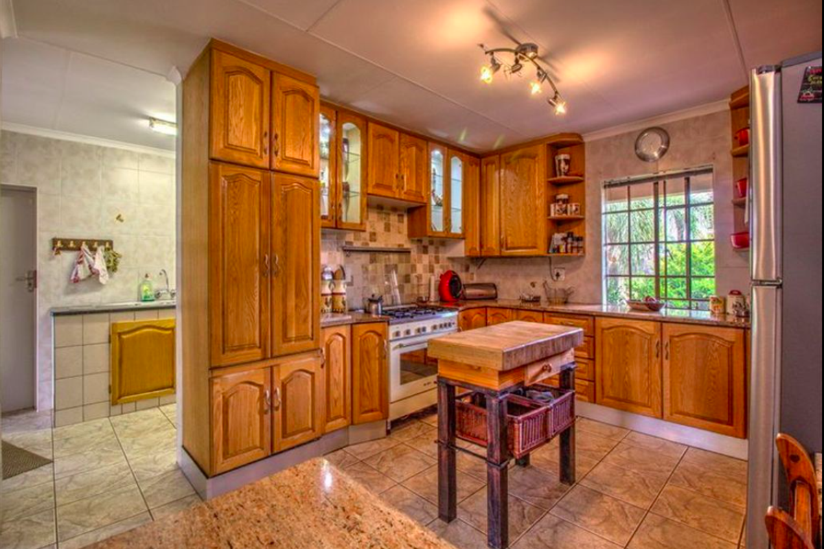 Traditional kitchen featuring warm wooden cabinetry, granite countertops, tiled flooring, and a gas stove, with an adjacent scullery area visible.
