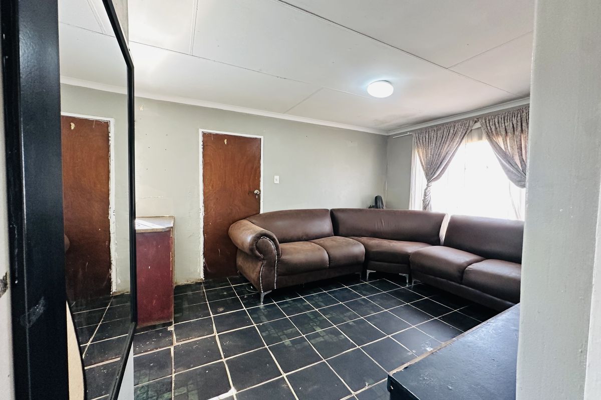 A living room featuring dark tiled flooring, timber doors, and a flush mount ceiling light, requiring cosmetic updates to improve its overall condition.