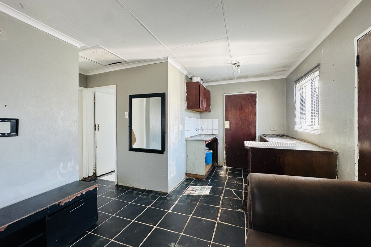 A dated kitchen area featuring dark tiled flooring, basic cabinetry, and a tiled backsplash, requiring renovation to modernize the space.