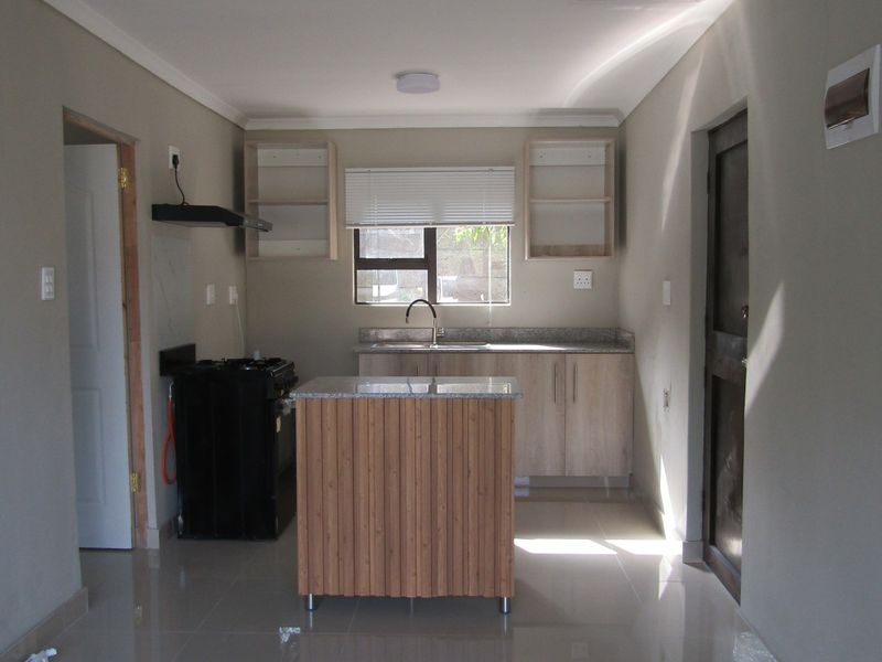 A functional kitchen featuring light wood cabinetry, granite countertops, a central island, and tiled flooring, offering a clean and neutral space for culinary activities.