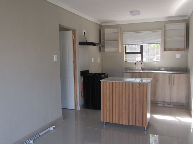 A clean, modern kitchen featuring light wood cabinetry, granite countertops, a central island, and tiled flooring in a bright, open-plan layout.