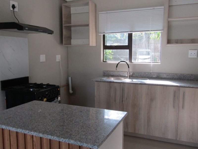 A clean, modern kitchen featuring granite countertops, light wood-finish cabinetry, a gas stove with extractor fan, and a stainless steel sink.