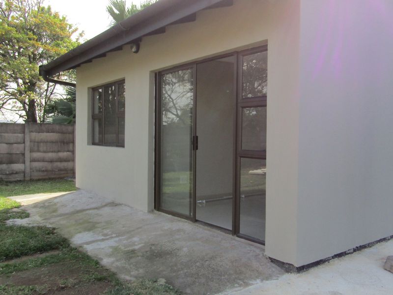 Rear view of the cottage featuring a concrete patio, sliding glass doors, and aluminium window frames, set against a private garden with boundary walling.
