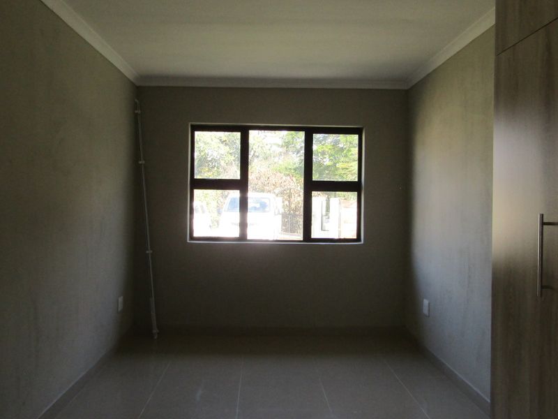 A clean, empty bedroom featuring neutral tiled flooring, built-in cupboards, and a large window providing natural light.
