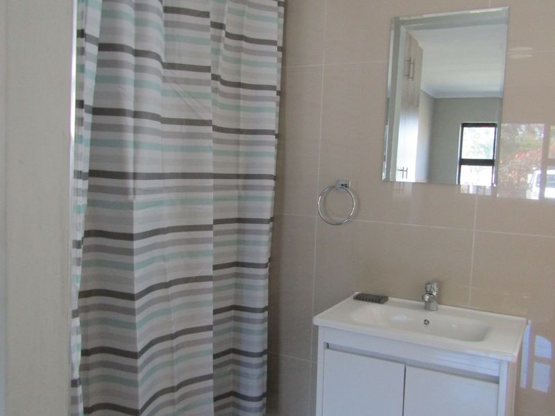 A functional bathroom featuring a modern vanity cabinet with basin, wall-mounted mirror, and a shower area with tiled walls.