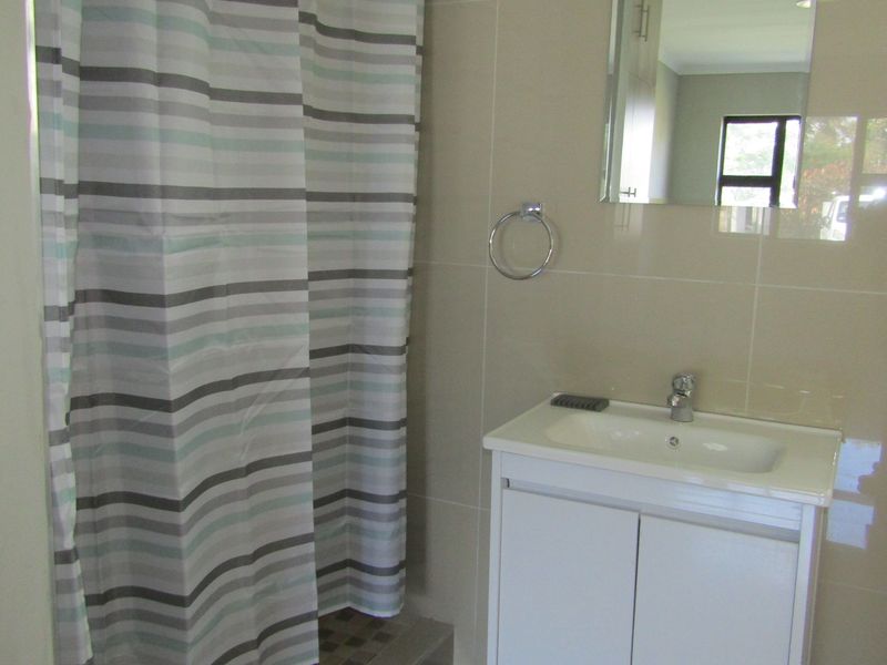 A functional bathroom featuring a modern vanity cabinet, wall-mounted mirror, and a tiled shower area with a neutral color palette.