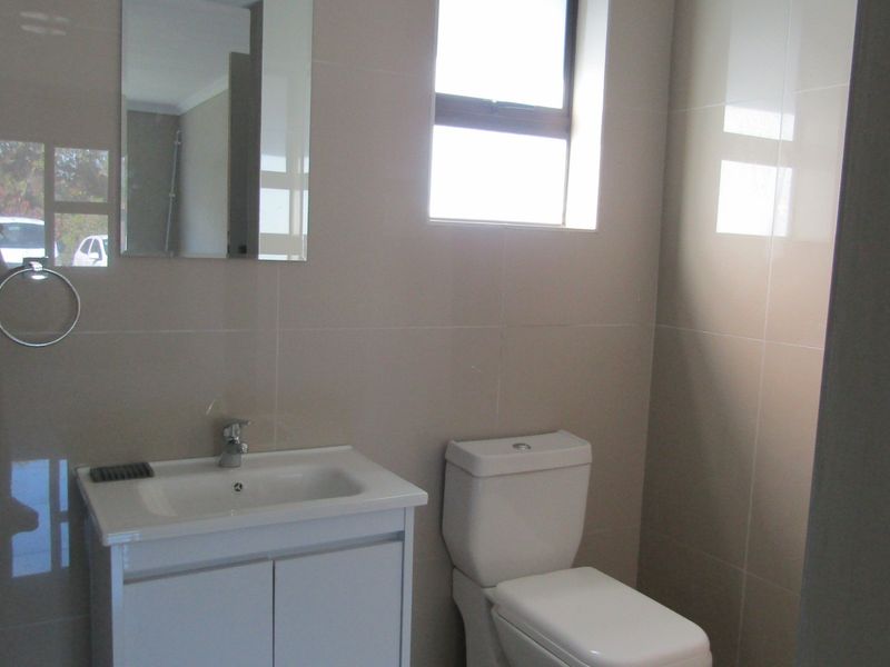 A clean, modern bathroom featuring neutral wall tiles, a white vanity cabinet with basin, and a dual-flush toilet.