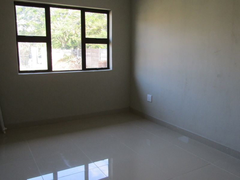 A clean, empty bedroom featuring neutral tiled flooring and a large aluminium-framed window, providing a blank canvas for interior design.