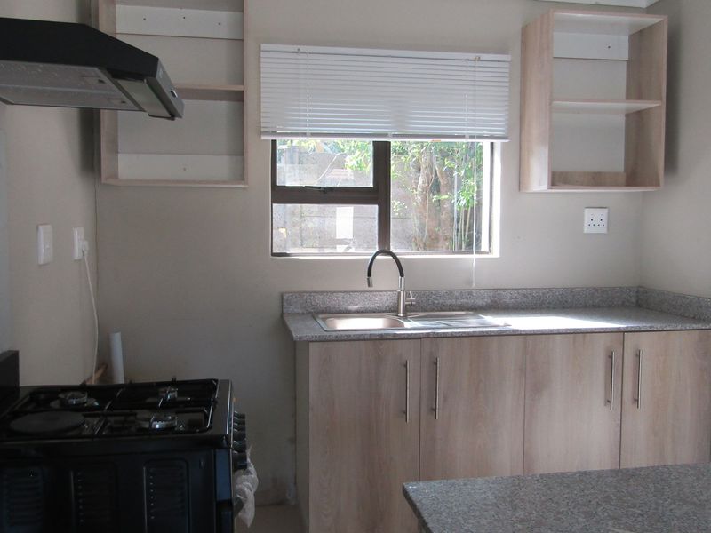 A functional kitchen featuring light wood cabinetry, granite countertops, a double sink, and a gas stove with an overhead extractor fan.