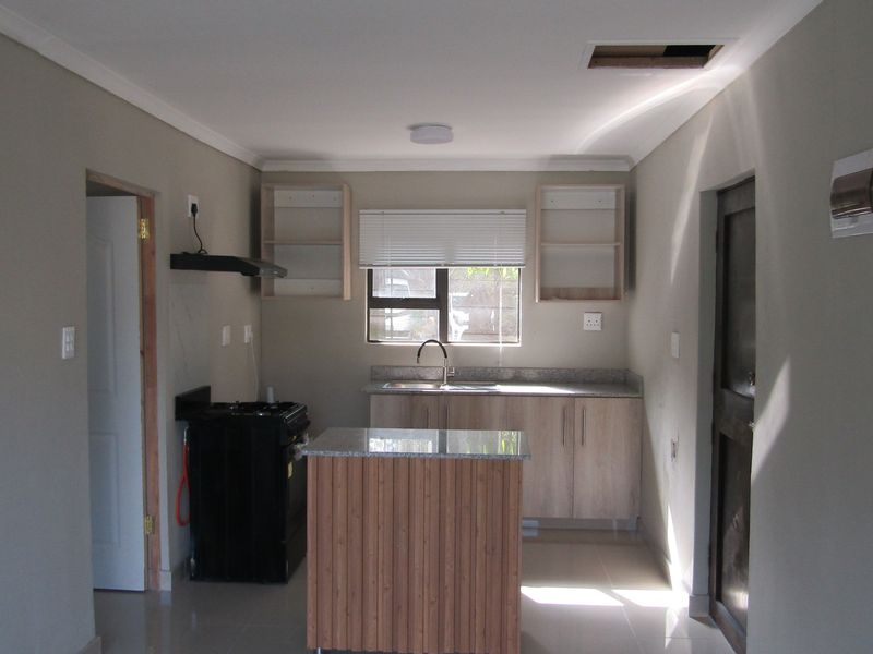 A functional kitchen featuring light wood cabinetry, granite countertops, a stainless steel sink, and a freestanding stove, with a neutral color palette throughout.