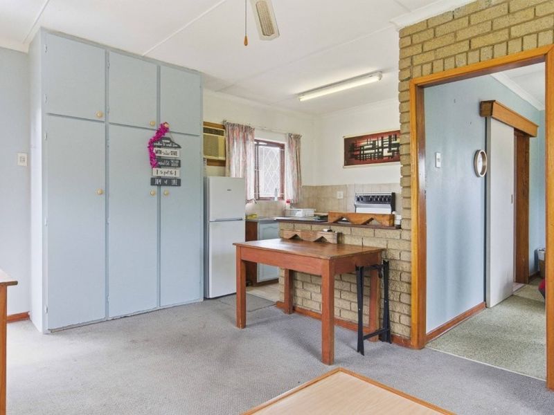 Open plan living and kitchen area featuring a brick feature wall, built-in cabinetry, and carpet flooring in a dated cottage style.