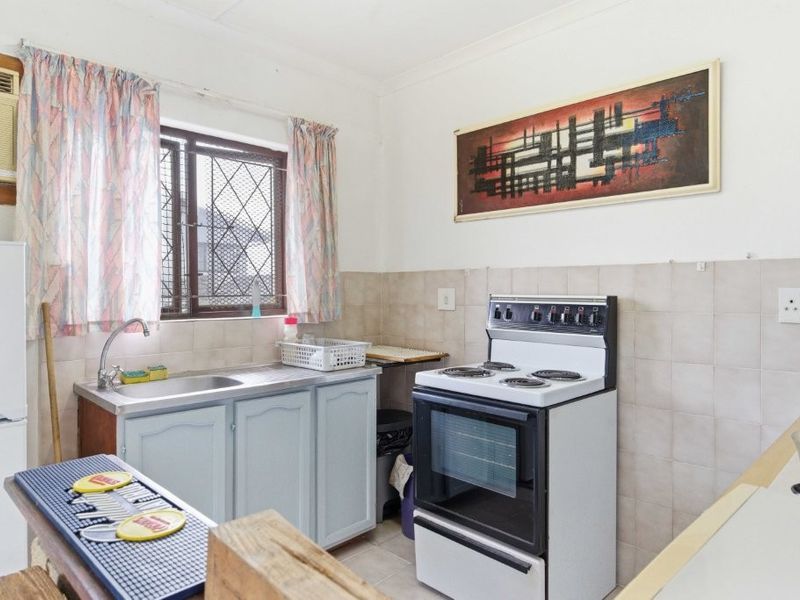 A functional kitchen featuring a stainless steel sink, tiled splashback, and a freestanding stove, with security bars on the window.