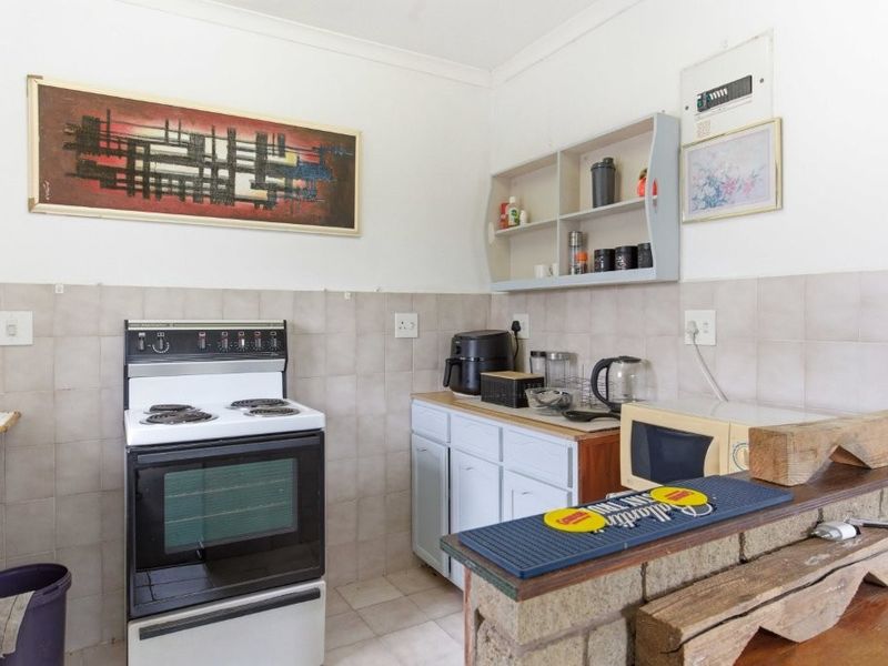 A compact kitchen featuring a freestanding stove, tiled backsplash, base cabinetry, and a rustic brick breakfast bar, offering potential for modernization.