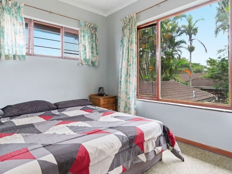 A bedroom featuring carpet flooring, timber-framed windows with security screens, and views of the surrounding garden and neighborhood.