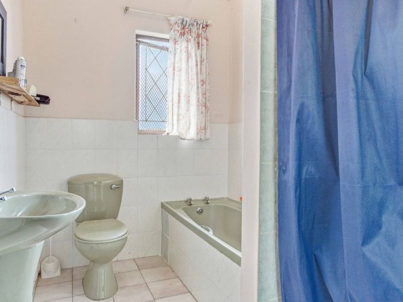 A dated bathroom featuring a pedestal basin, toilet, and bathtub with tiled finishes, requiring modernization to improve its aesthetic appeal and functionality.