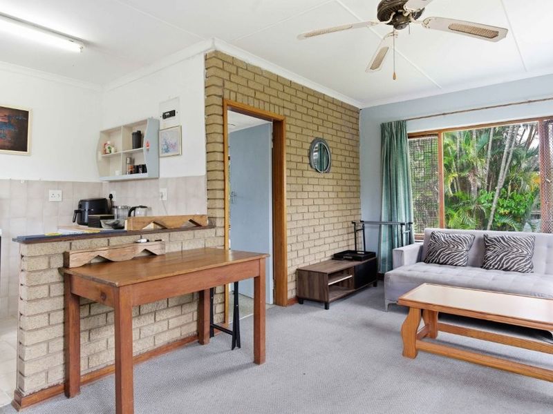Open plan living area featuring an exposed brick feature wall, ceiling fan, and an adjoining kitchen space with tiled splashbacks.