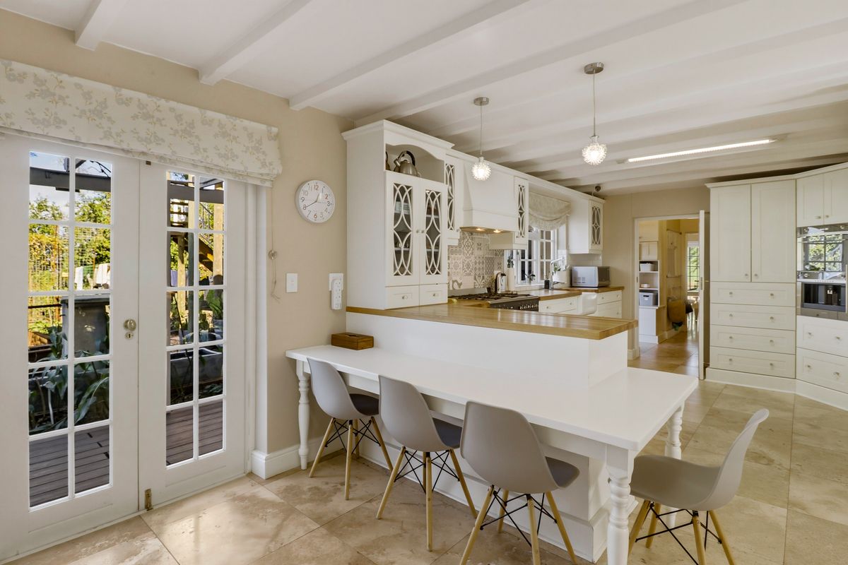 A bright, well-appointed kitchen featuring white cabinetry, timber countertops, a gas hob, and direct access to the outdoor patio through French doors.