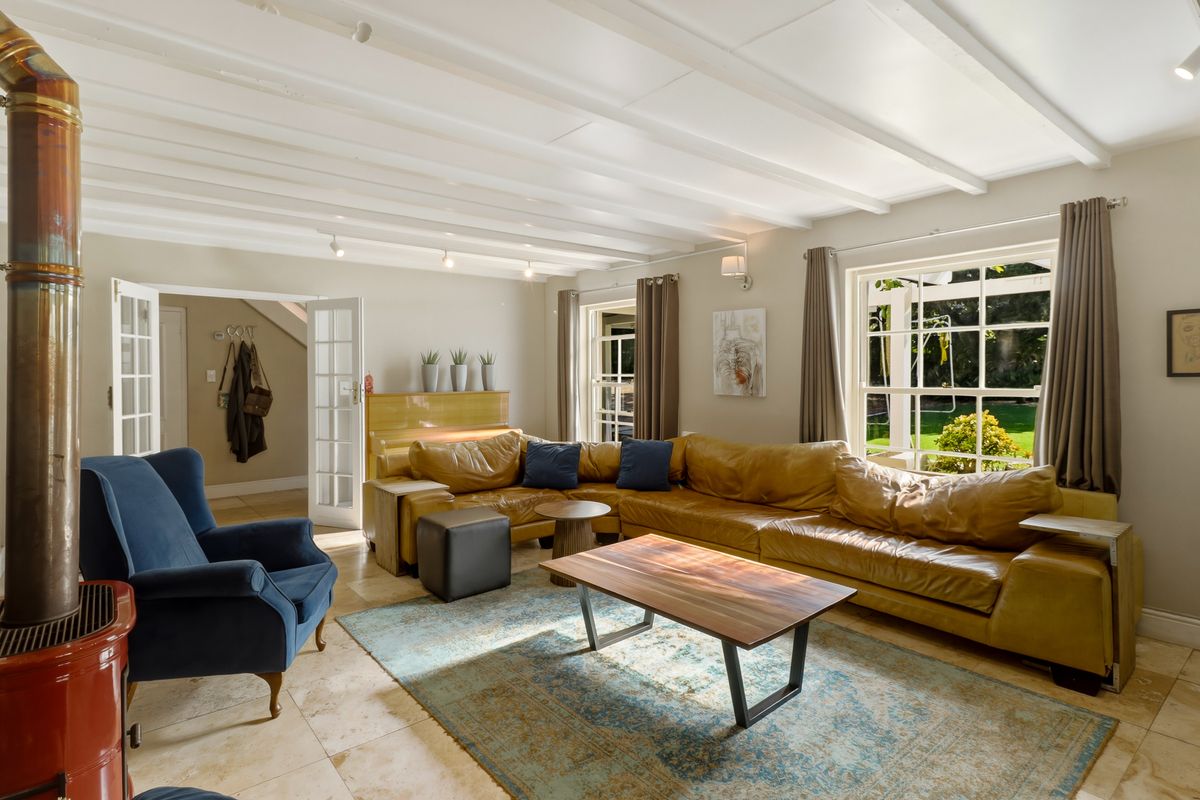 Spacious living room featuring exposed beam ceilings, stone tile flooring, and a characterful freestanding fireplace, with direct access to the garden through french doors.