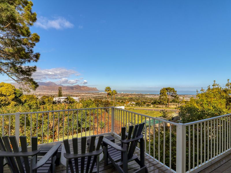 Elevated timber balcony featuring a white metal balustrade, offering expansive panoramic views of the surrounding landscape and distant coastline.