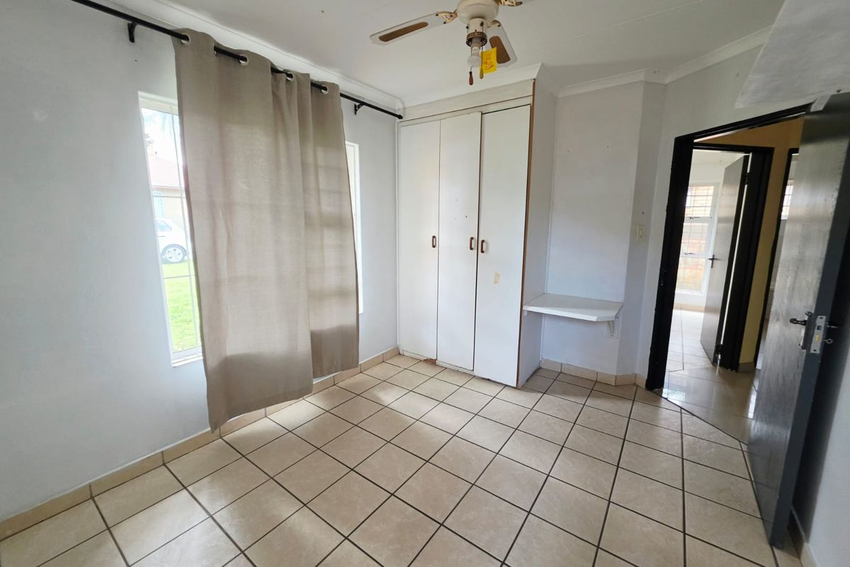 A vacant bedroom featuring tiled flooring, built-in cupboards, a built-in desk, and a ceiling fan, offering a functional space ready for personalization.