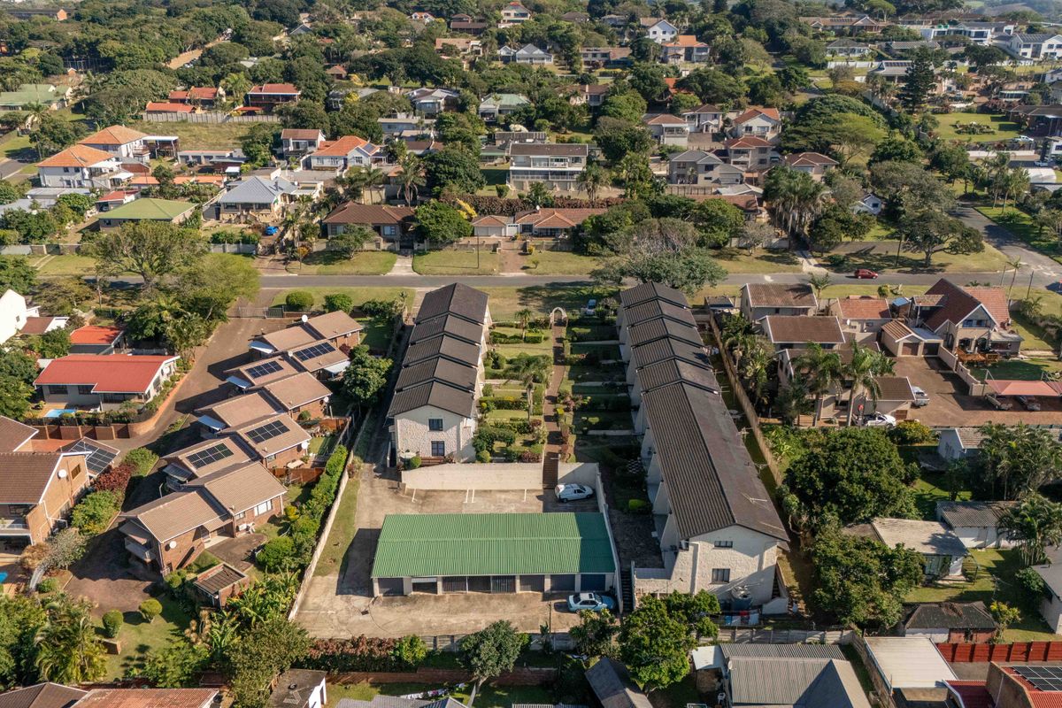Aerial view of a townhouse complex featuring two residential blocks, a central garden area, and a dedicated garage block with paved driveway access.