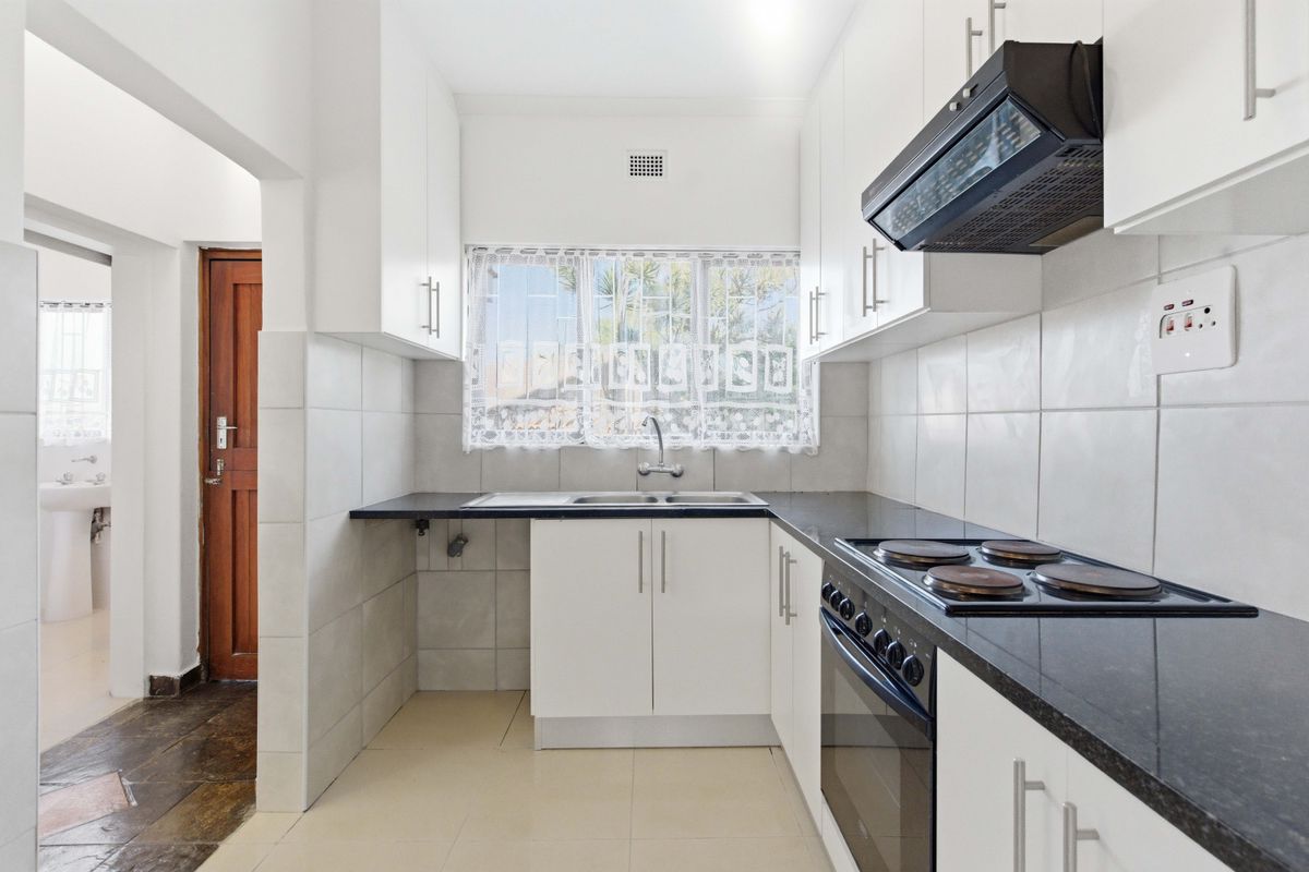 A clean, functional kitchen featuring white cabinetry, dark stone countertops, built-in oven and stove, and tiled splashbacks, offering a bright and practical workspace.