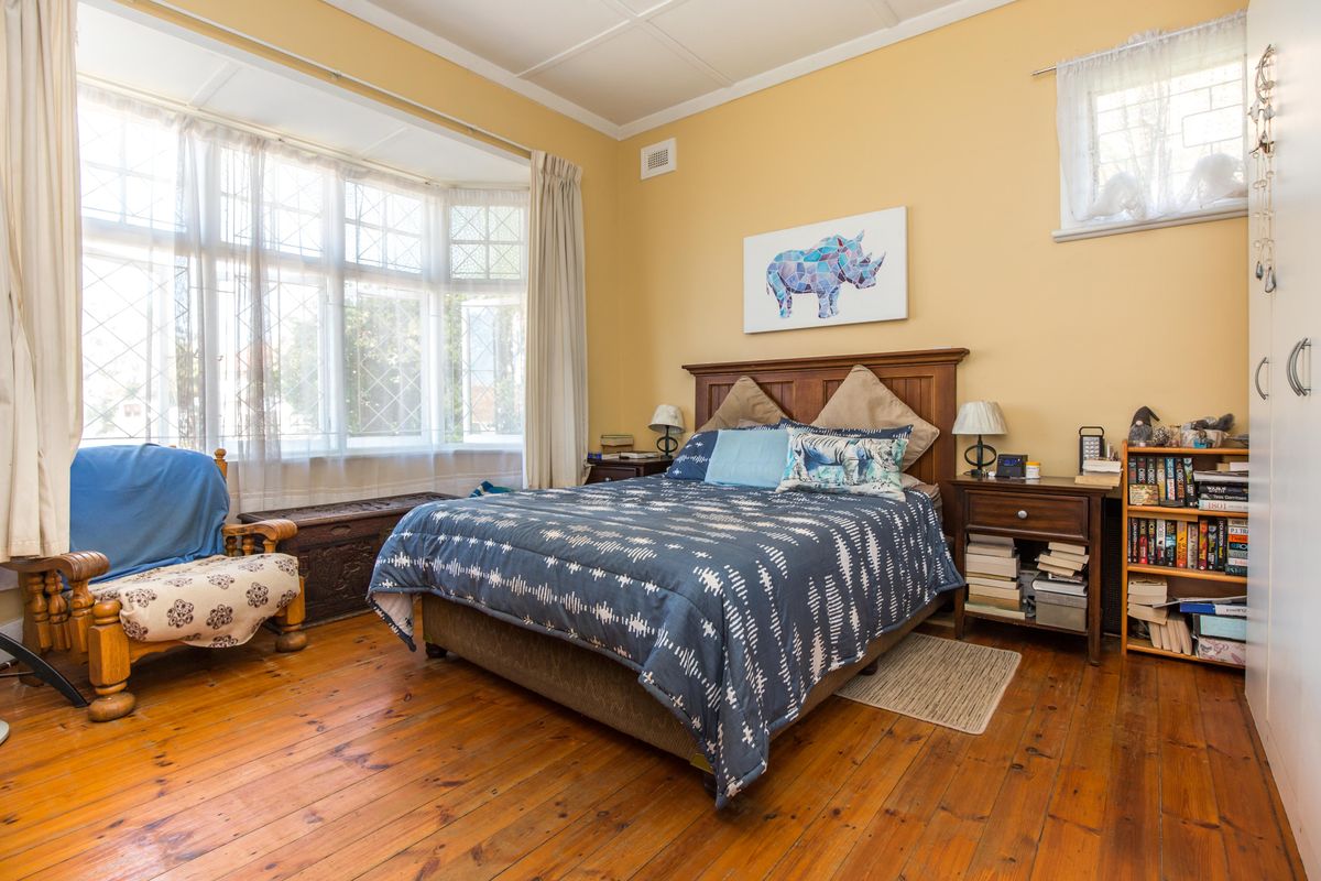 A bedroom featuring original timber flooring, a large bay window with leadlight detailing, and built-in wardrobe storage.