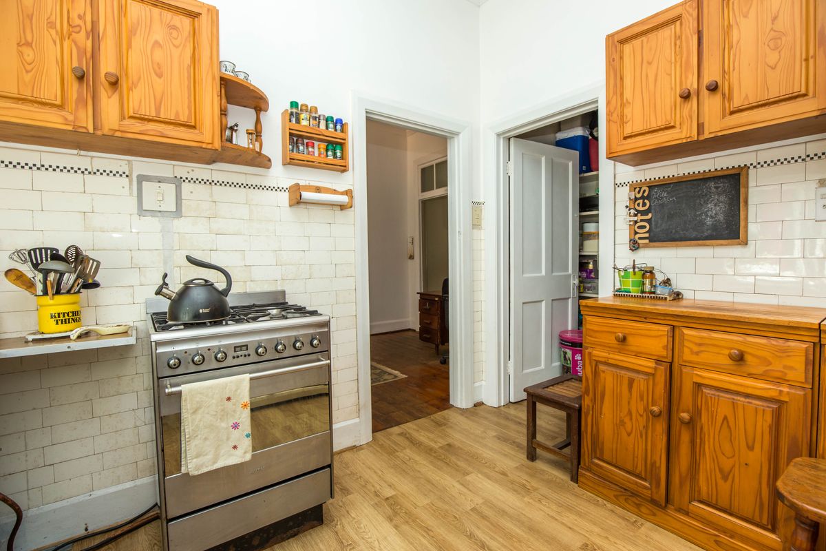A functional kitchen featuring timber cabinetry, subway-style wall tiling, and a freestanding gas stove, with an adjacent pantry or scullery area.