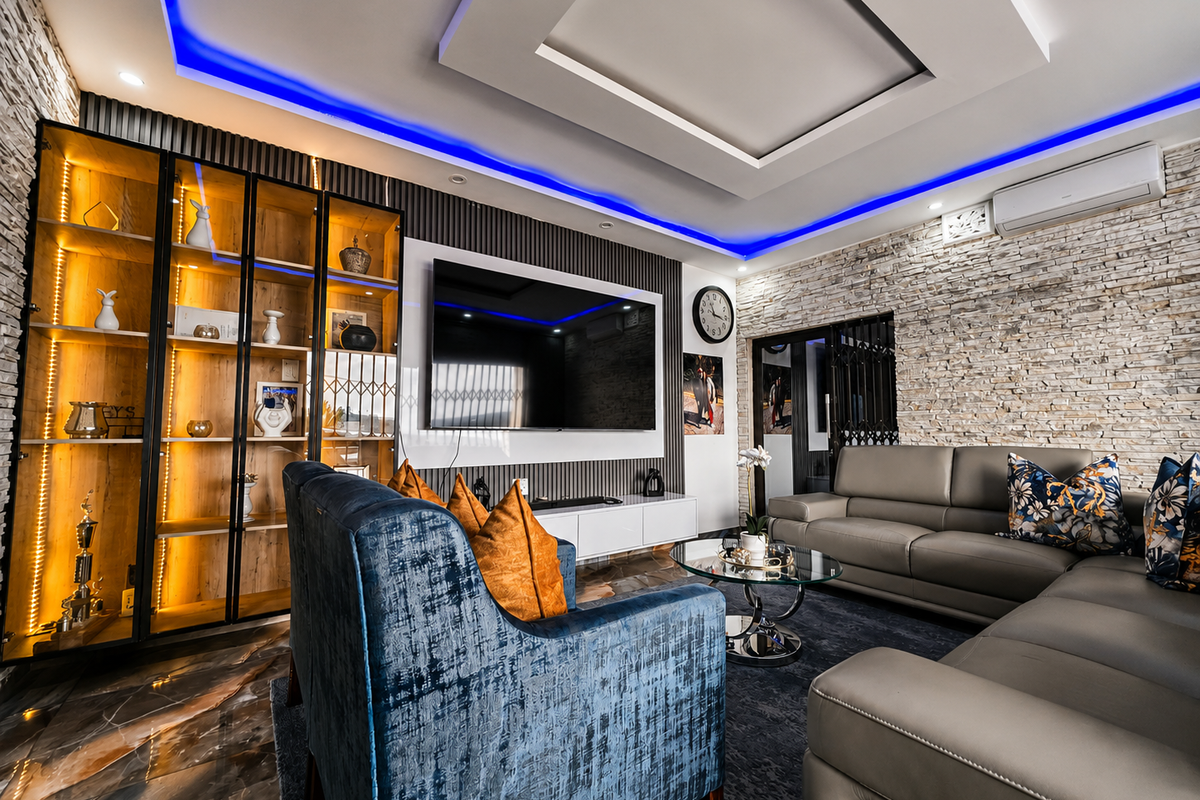 Modern living room featuring a stone veneer accent wall, recessed ceiling with ambient LED lighting, built-in display cabinetry, and sleek tiled flooring.