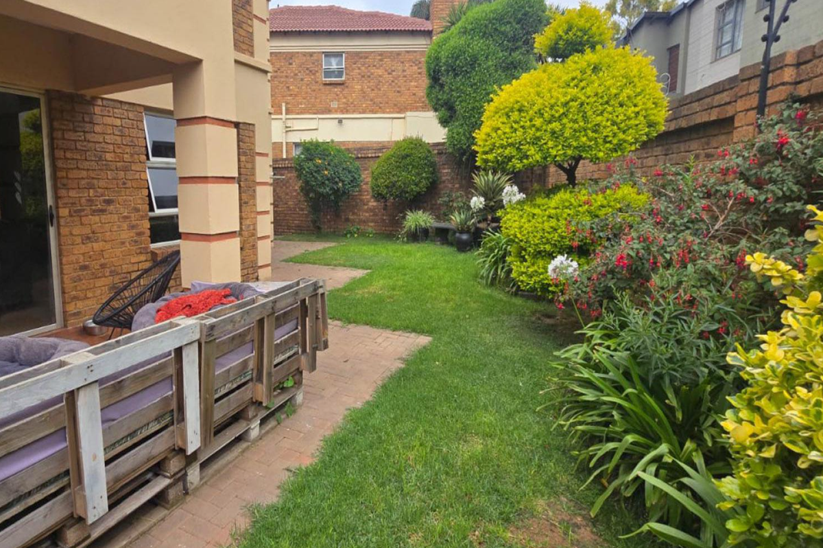 A private rear garden featuring a paved patio area, established landscaping, and brick boundary walls, providing a pleasant outdoor space for the townhouse.