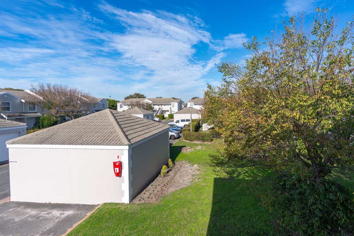 An elevated view of the apartment complex grounds, featuring a detached garage structure, paved driveway, and surrounding landscaped garden areas.