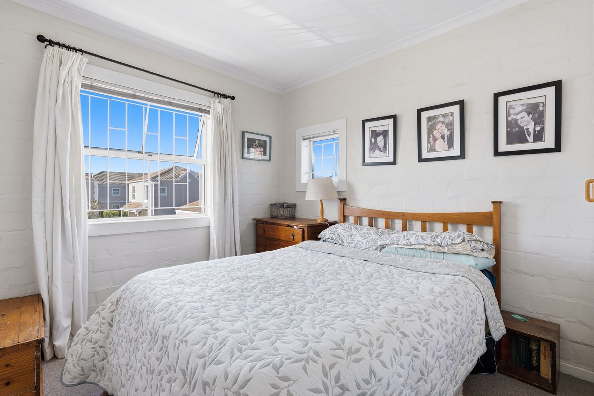 A bright bedroom featuring painted brick walls, coved ceilings, and security-fitted windows, offering a clean and functional living space.
