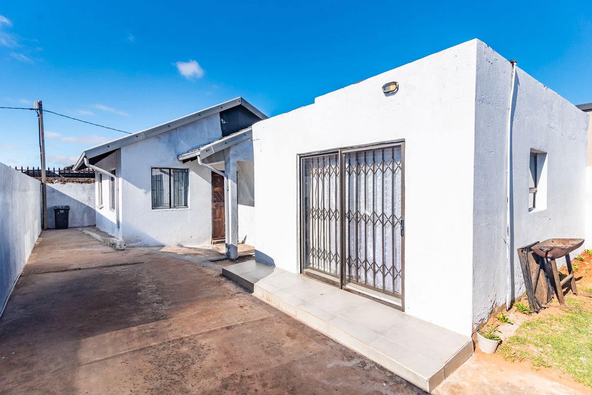 Rear exterior view of the property featuring a concrete driveway, tiled patio area, and sliding security gate access.
