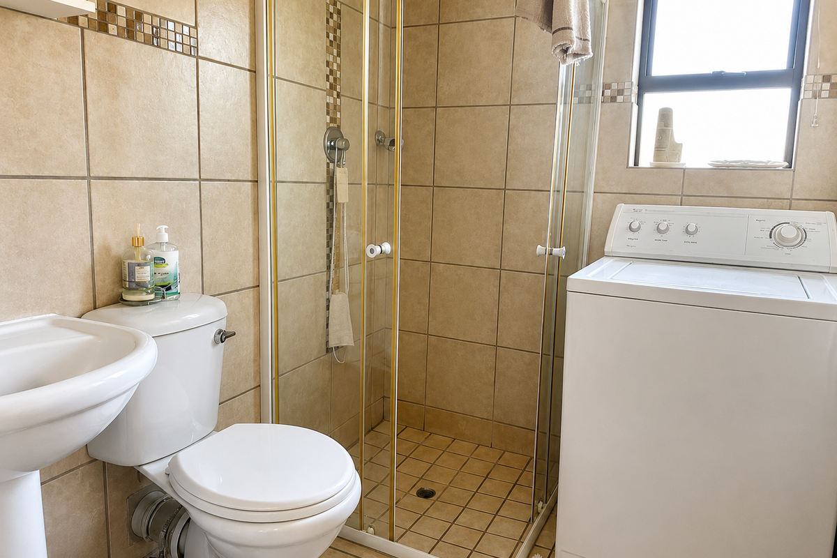 A functional bathroom featuring a pedestal basin, toilet, and a glass-enclosed shower with neutral wall and floor tiling.