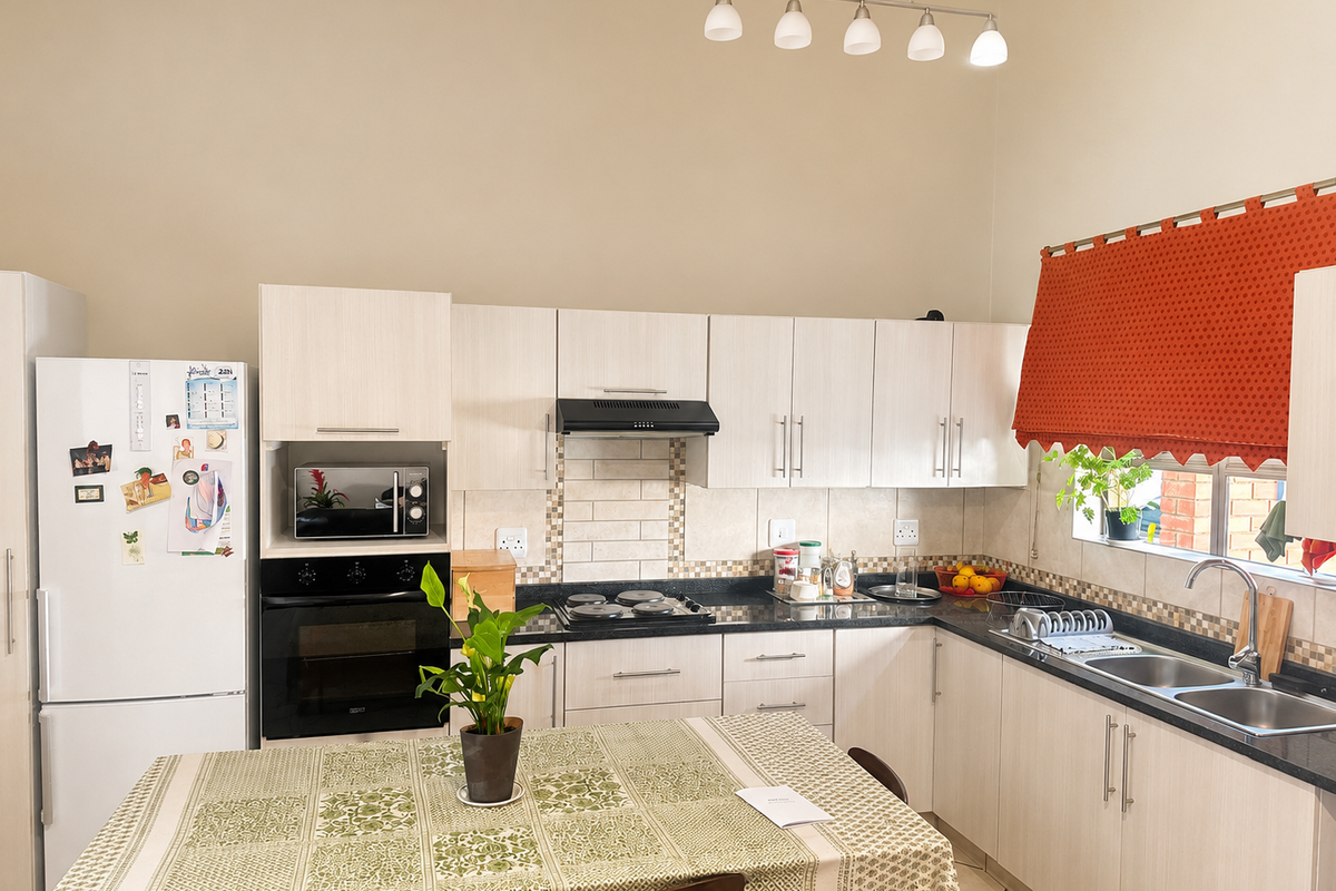 A functional kitchen featuring light-toned cabinetry, granite countertops, a built-in oven with hob, and a double basin sink with a tiled backsplash.