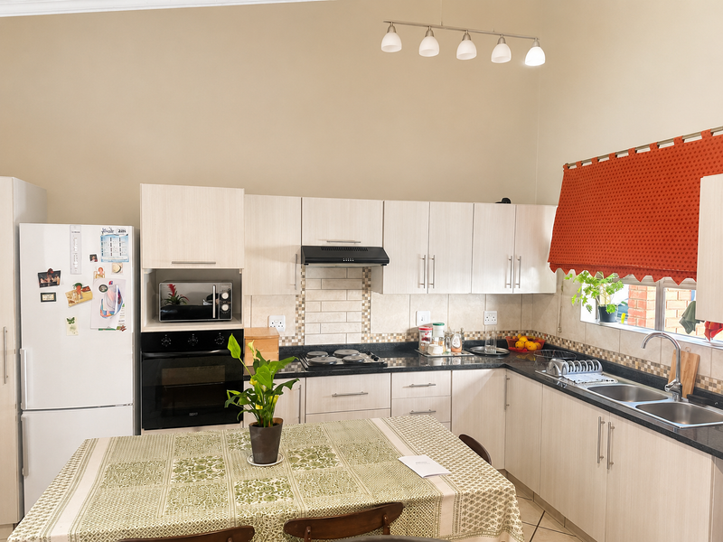 A functional kitchen featuring light-toned cabinetry, granite countertops, a built-in oven with hob, and a double basin sink with a tiled backsplash.