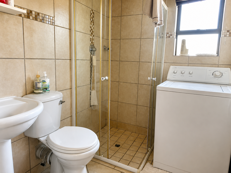 A functional bathroom featuring a pedestal basin, toilet, and a glass-enclosed shower with neutral wall and floor tiling.