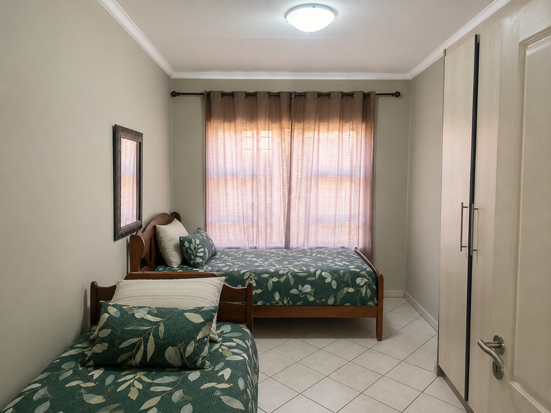 A well-maintained bedroom featuring tiled flooring, a built-in wardrobe, and natural light through a window with curtain fittings.