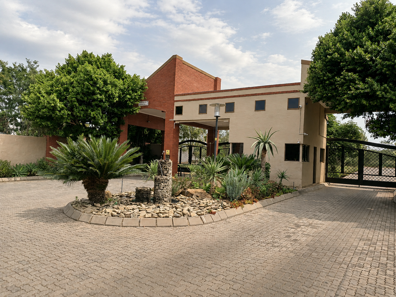 The front entrance of the property features a paved driveway, a brick and rendered facade, a security gate, and a landscaped garden with a water feature.