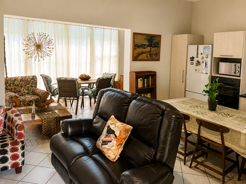Open-plan living and kitchen area featuring tiled flooring, built-in cabinetry, and integrated kitchen appliances, with direct access to a sunlit patio area.