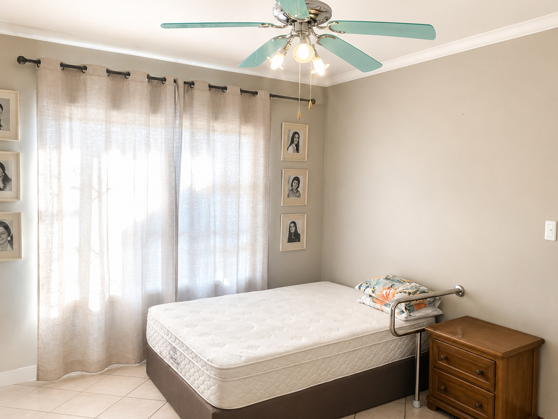 A well-maintained bedroom featuring neutral wall tones, tiled flooring, and a functional ceiling fan with integrated lighting.