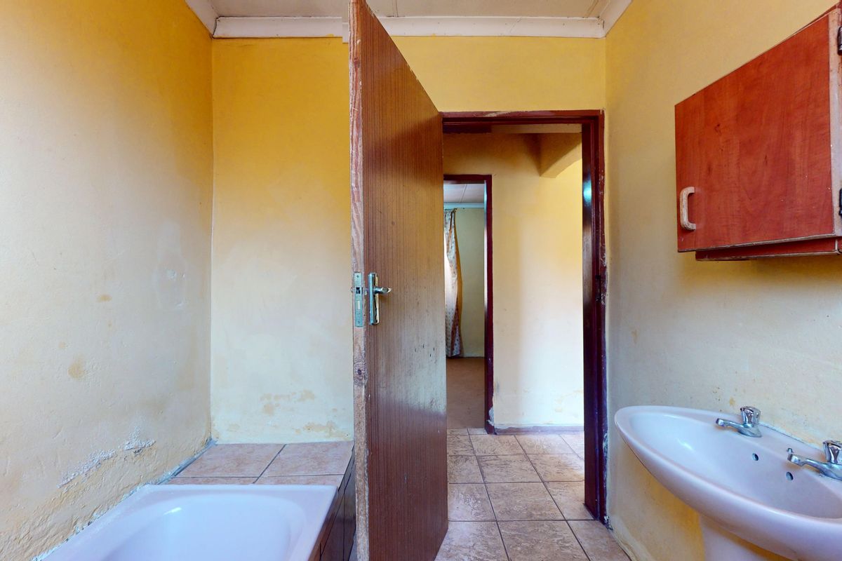A dated bathroom featuring a pedestal basin, bathtub, and tiled flooring, requiring cosmetic updates to modernize the space.