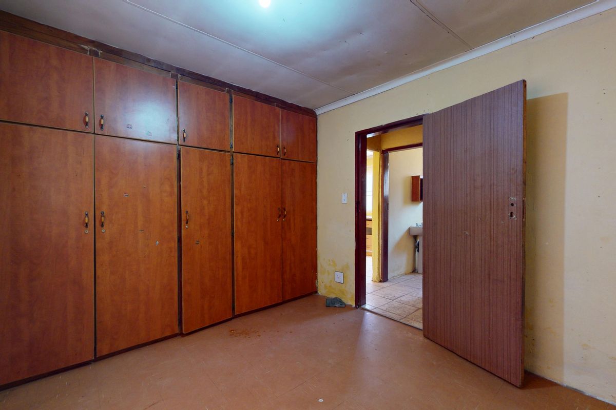 An empty bedroom featuring built-in wooden cupboards, showing signs of wear and requiring cosmetic updates to the walls and ceiling.